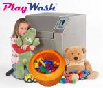 Rotaļlietu mazgāšanas mašīna ar sudraba korpusu, blakus bērns, mīkstās rotaļlietas un oranža groza ar rotaļlietām.